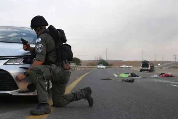 Un soldado israelí se refugia detrás de un automóvil después de que los terroristas de Hamás ingresaron al sur de Israel y mataron a civiles. Aquí se ven cuerpos israelíes en una carretera principal cerca del kibutz Gevim de Israel, cerca de la frontera con Gaza, el 7 de octubre de 2023. (Oren Ziv/AFP vía Getty Images)
