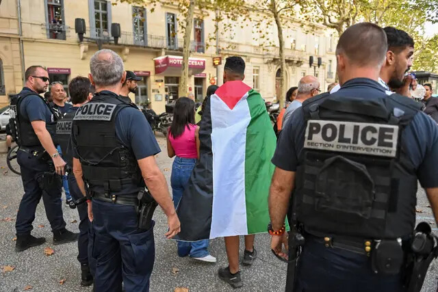 Un manifestante envuelto en una bandera palestina camina frente a agentes de la policía francesa durante una concentración no autorizada en Nimes, al sur de Francia, el 11 de octubre de 2023 (Sylvain Thomas/AFP via Getty Images)