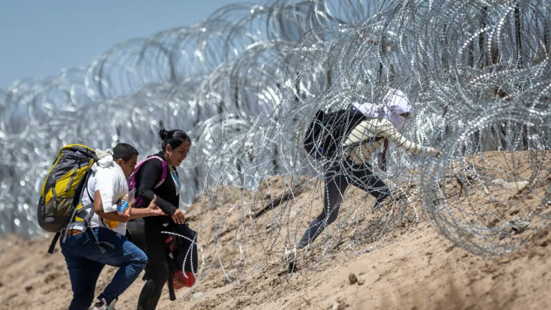 Inmigrantes ilegales caminan a través de alambre de púas mientras cruzan la frontera desde México, en El Paso, Texas, el 11 de mayo de 2023. (John Moore/Getty Images)