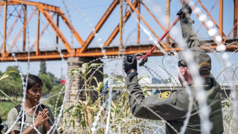 Un migrante de Venezuela ora mientras espera que un agente de la Patrulla Fronteriza de Estados Unidos corte el alambre de púas después de cruzar el Río Grande hacia Eagle Pass, Texas, el 24 de septiembre de 2023. (Andrew Caballero-Reynolds/AFP vía Getty Images)
