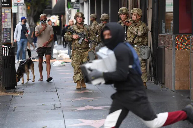 Un saqueador que lleva cajas de zapatos pasa corriendo junto a soldados de la Guardia Nacional en Hollywood, California, el 1 de junio de 2020. (Robyn Beck/AFP vía Getty Images)