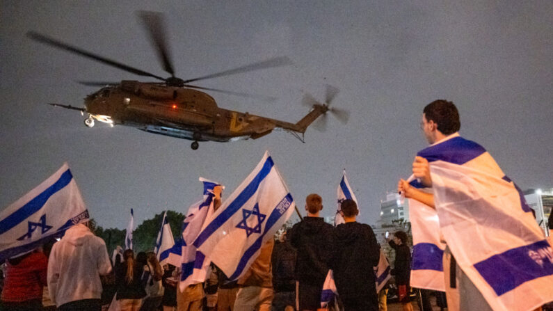 La gente agita banderas y aplaude mientras un segundo helicóptero con rehenes israelíes liberados anteriormente por Hamás aterriza en el centro médico Schneider en el tercer día de la tregua temporal donde desembarcaron detrás de pantallas mientras familiares y amigos esperan cerca el 26 de noviembre de 2023 en Petah Tikva, Israel. (Alexi J. Rosenfeld/Getty Images)