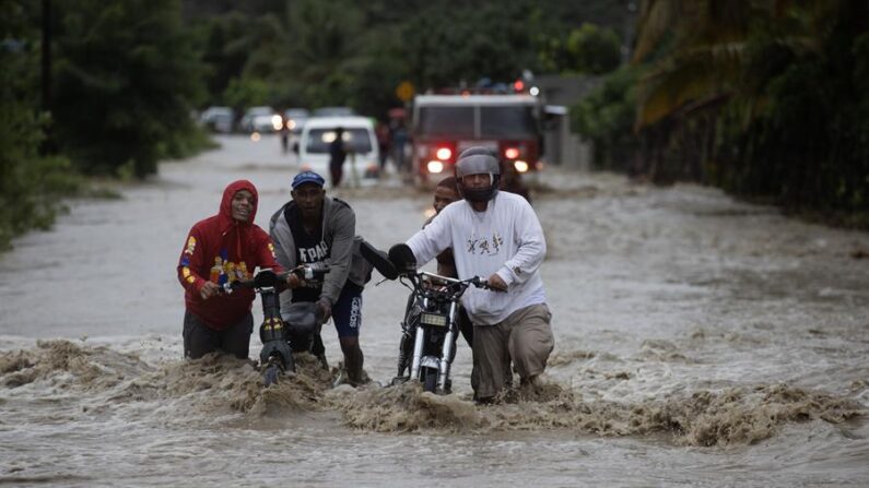 Personas cruzan con dificultad la carretera que se encuentra inundada producto de las intensas lluvias, el 18 de noviembre 2023 en San José de Ocoa (República Dominicana). EFE/Orlando Barría