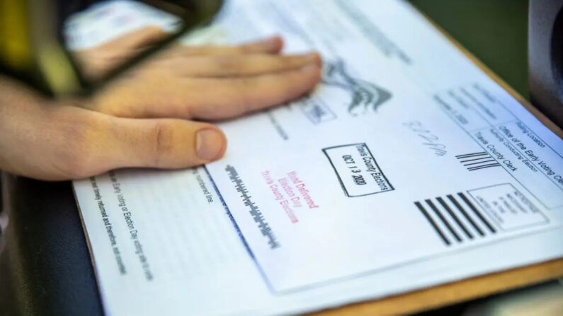  Un trabajador electoral sella la papeleta de un votante antes de depositarla en una urna segura en un punto de entrega de papeletas en Austin, Texas, el 13 de octubre de 2020. (Sergio Flores/Getty Images)
