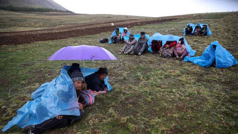 Campesinos descansan bajo la lluvia durante la faena de volteo de la tierra de cultivo, en San José de Apata, provincia de Jauja (Perú). EFE/Paolo Aguilar