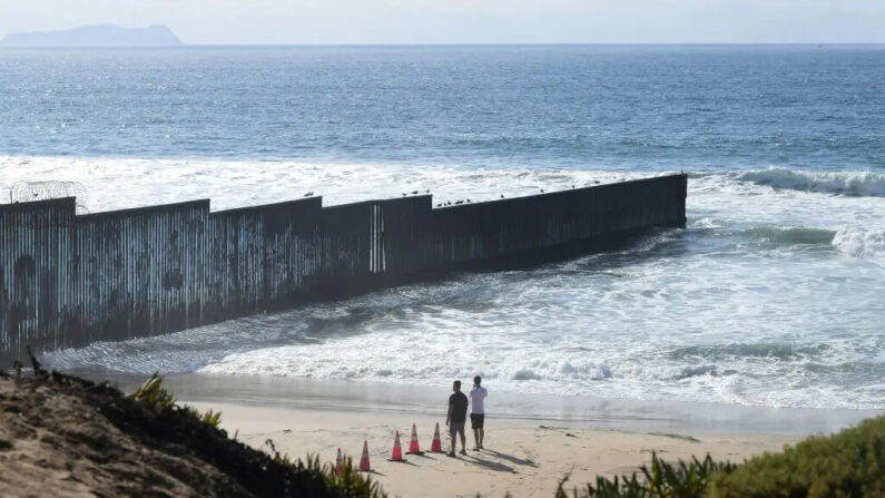 Varias personas miran hacia la valla fronteriza entre Estados Unidos y México que se adentra en el océano Pacífico, vista desde Imperial Beach, a las afueras de San Diego, en el extremo suroeste del país, el 7 de noviembre de 2021. (Frederic Brown/AFP vía Getty Images)