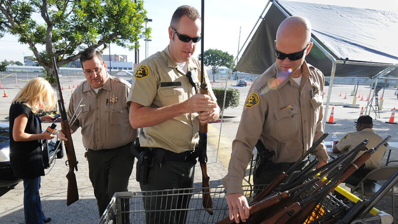 Agentes del Sheriff del condado de Los Ángeles de la comisaría de Lennox añaden rifles a un arsenal durante un intercambio de "armas por tarjetas de regalo" en el centro sur de Los Ángeles el 4 de diciembre de 2009. (Mark Ralston/AFP vía Getty Images)