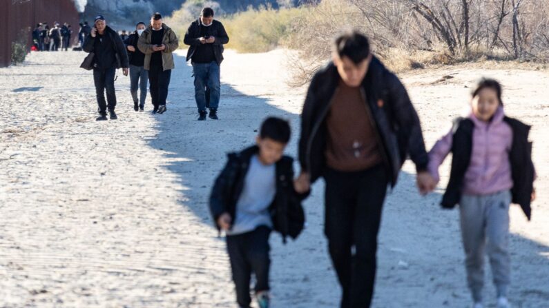 Migrantes caminan a lo largo del lado estadounidense del muro fronterizo de Estados Unidos el 6 de diciembre de 2023. (John Fredricks/The Epoch Times)