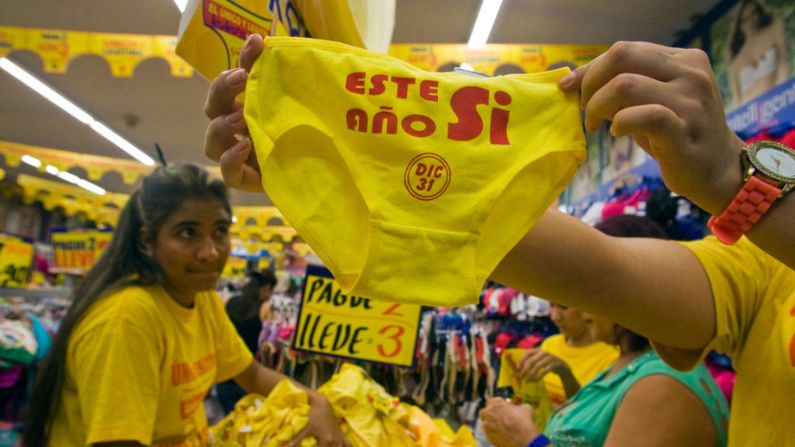 Una vendedora muestra unas bragas amarillas que dicen "Sí, este año", usadas por superstición para el Año Nuevo, en una tienda de Medellín, Colombia, el 30 de diciembre de 2014. En gran parte de América Latina, el Año Nuevo se celebra con augurios profundamente arraigados como espigas y flores amarillas, baños de hierbas y champagne, caminar por la cuadra con una maleta, tener lentejas en el bolsillo, poner papas debajo de la cama y el ritual de las 12 uvas. (FREDY AMARILES GARCÍA/AFP vía Getty Images)