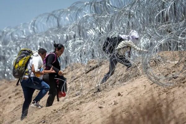 Inmigrantes ilegales caminan a través del alambre de púas que rodea un campamento improvisado de migrantes después de cruzar la frontera desde México, en El Paso, Texas, el 11 de mayo del 2023. (John Moore/Getty Images)