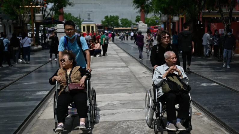 Un anciano y una anciana son empujados en silla de ruedas por una calle de Beijing el 11 de mayo de 2021. (Wang Zhao/AFP vía Getty Images)