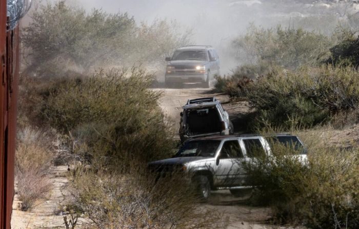 Presuntos miembros del cártel mexicano conducen camionetas SUV con docenas de inmigrantes ilegales a una brecha abierta en el muro fronterizo de EE. UU. cerca de Jacomba, California, el 6 de diciembre de 2023. (John Fredricks/The Epoch Times)