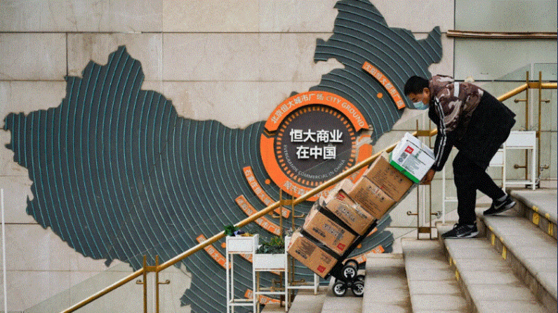 Un trabajador empuja un carro delante de un cartel que muestra la operación de Evergrande Group en China en un complejo de viviendas de la promotora inmobiliaria en Pekín el 8 de diciembre de 2021. (Noel Celis/AFP vía Getty Images)