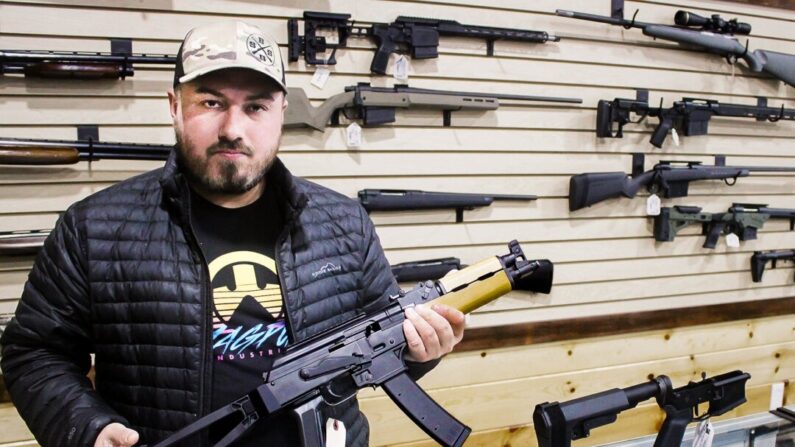 Justin Barrett, propietario de Barrett Outdoors en Durant, Oklahoma, muestra una pistola AK con un soporte estabilizador. En el mostrador junto a él hay un soporte similar para una pistola AR-15. (Michael Clements/The Epoch Times)