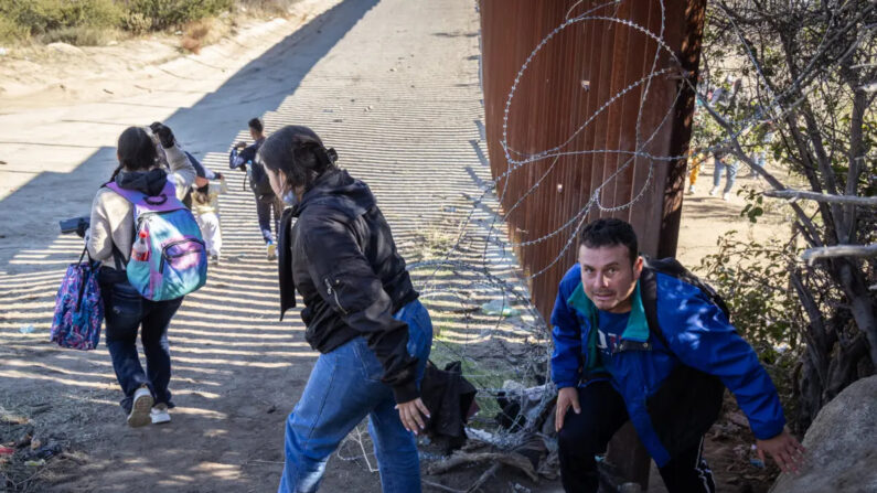 Inmigrantes ilegales pasan a través de una brecha en el muro fronterizo de Estados Unidos a la espera de ser procesados por agentes de la Patrulla Fronteriza en Jacumba, California, el 7 de diciembre de 2023. (John Fredricks/The Epoch Times)