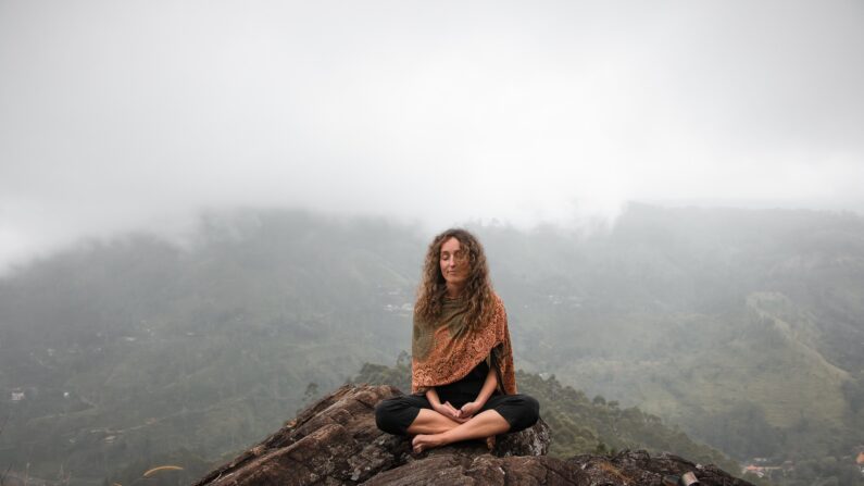 Una mujer meditando en la cúspide de una montaña. (vined mind/Pixabay)