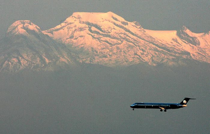 Fotografía tomada el 25 de octubre de 2007 desde la Torre Latinoamericana de Ciudad de México de un avión de pasajeros volando al atardecer frente al volcán extinto Iztaccíhuatl, cubierto de nieve, a 120 km al este de la capital. (LUIS ACOSTA/AFP vía Getty Images)