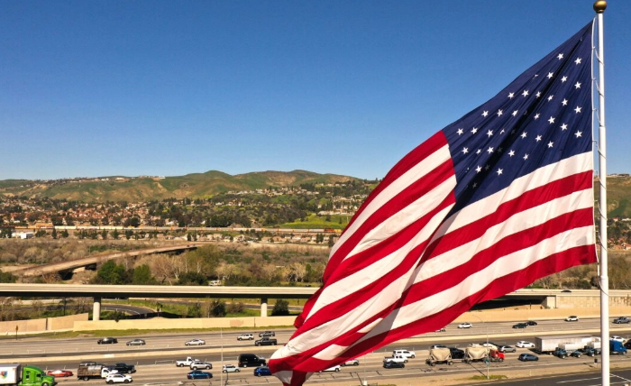 Coches y camiones pasan junto a una bandera estadounidense en la autopista 91 en Anaheim Hills, California, el 8 de febrero de 2023. (Patrick T. Fallon/AFP vía Getty Images)