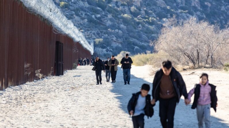 Migrantes caminan a lo largo del lado estadounidense del muro fronterizo de Estados Unidos después de cruzar una brecha en Jacumba, California, el 6 de diciembre de 2023. (John Fredricks/The Epoch Times)