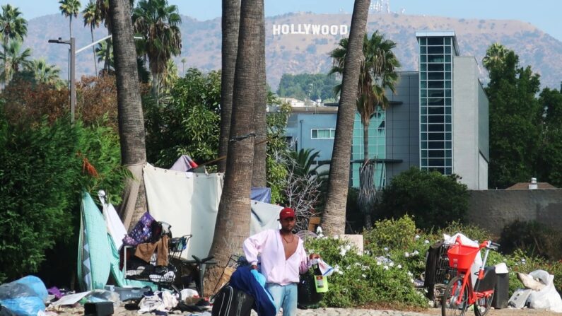 Un hombre se encuentra frente a un campamento para personas sin hogar, con el letrero de Hollywood al fondo, en Los Ángeles, California, el 23 de septiembre de 2019. (Mario Tama/Getty Images)
