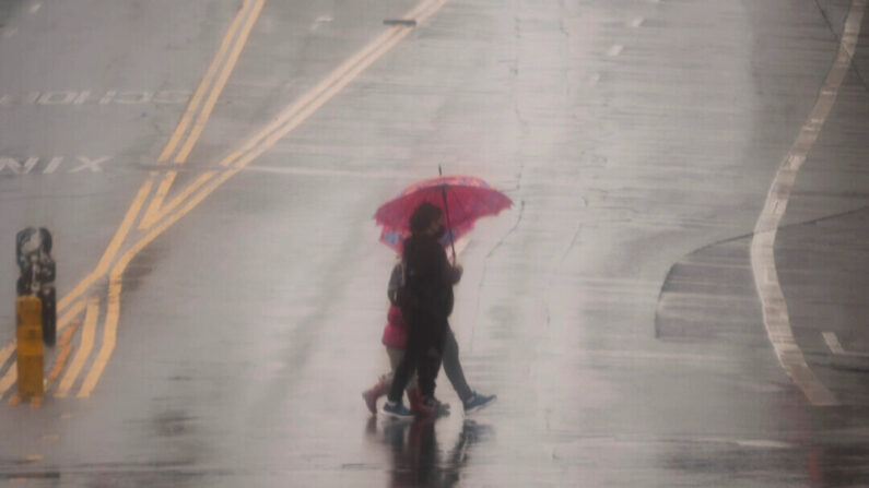 La gente cruza la calle con paraguas bajo una fuerte lluvia en Los Ángeles, el 19 de febrero de 2024. (Damian Dovarganes/AP)

