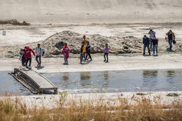 Migrantes cruzan el río Tijuana y avanzan hacia el muro fronterizo de Estados Unidos en Tijuana, México, el 11 de mayo de 2023. (John Fredricks/The Epoch Times)