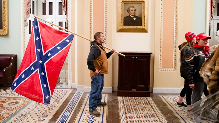 Un manifestante sostiene una bandera confederada frente a la Cámara del Senado durante una protesta tras irrumpir en el Capitolio estadounidense en Washington, DC, el 6 de enero de 2021. (SAUL LOEB / AFP)