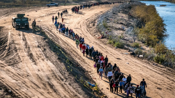 En esta vista aérea, un grupo de más de 1000 inmigrantes ilegales camina hacia un centro de procesamiento de campo de la Patrulla Fronteriza de EE.UU. después de cruzar el Río Grande desde México en Eagle Pass, Texas, el 18 de diciembre de 2023. (John Moore/Getty Images)