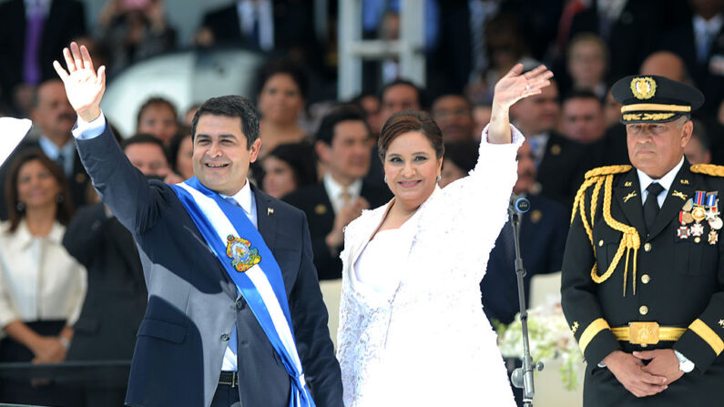 El expresidente de Honduras, Juan Orlando Hernández, flanqueado por su esposa Ana García, saluda al recibir la banda presidencial durante su toma de posesión el 27 de enero de 2014. (Orlando Sierra/AFP vía Getty Images)