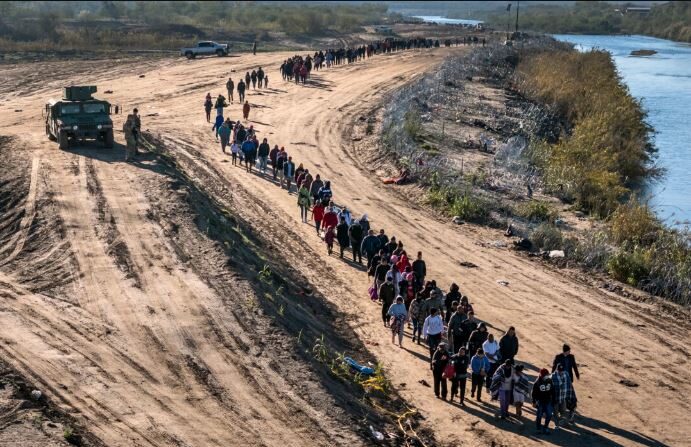 En esta vista aérea, un grupo de más de 1000 inmigrantes camina hacia un centro de procesamiento de campo de la Patrulla Fronteriza de EE. UU. después de cruzar el Río Grande desde México en Eagle Pass, Texas, el 18 de diciembre de 2023. (John Moore/Getty Images)