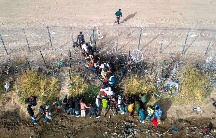 Inmigrantes ilegales atraviesan alambres de púas mientras cruzan la frontera entre México y Estados Unidos en El Paso, Texas, el 13 de marzo de 2024. (John Moore/Getty Images)
