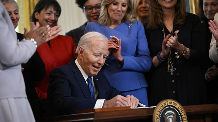 El presidente Joe Biden firma una orden ejecutiva destinada a impulsar el estudio de la salud de la mujer durante una recepción en honor del Mes de la Historia de la Mujer en la Sala Este de la Casa Blanca en Washington, el 18 de marzo de 2024. (Brendan Smialowski/AFP vía Getty Images)

