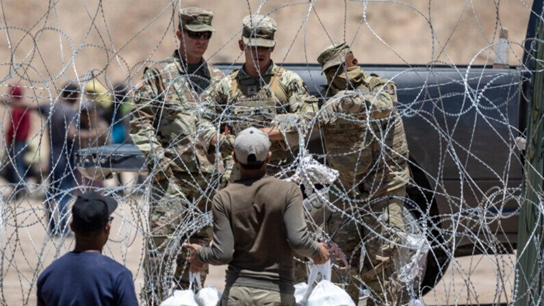 Soldados de la Guardia Nacional de Texas cierran una sección de alambre de púas que rodea un campamento de inmigrantes improvisado mientras un inmigrante ilegal intenta regresar con comida para su familia, en El Paso, Texas, el 11 de mayo de 2023. (John Moore/Getty Images)
