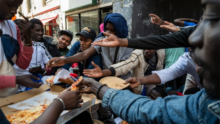Un policía reparte pizza a decenas de inmigrantes ilegales recién llegados a Nueva York mientras acampan frente al Hotel Roosevelt, el 1 de agosto de 2023. (Spencer Platt/Getty Images)
