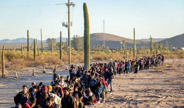 Inmigrantes ilegales hacen fila en un remoto centro de procesamiento de la Patrulla Fronteriza de EE.UU. después de cruzar la frontera entre EE. UU. y México, en Lukeville, Arizona, el 7 de diciembre de 2023. (John Moore/Getty Images)