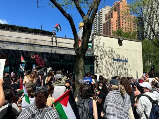Un estudiante ondea la bandera palestina desde el techo del campus de la Universidad Fordham en Manhattan el 1 de mayo de 2024. (Juliette Fairley/The Epoch Times)