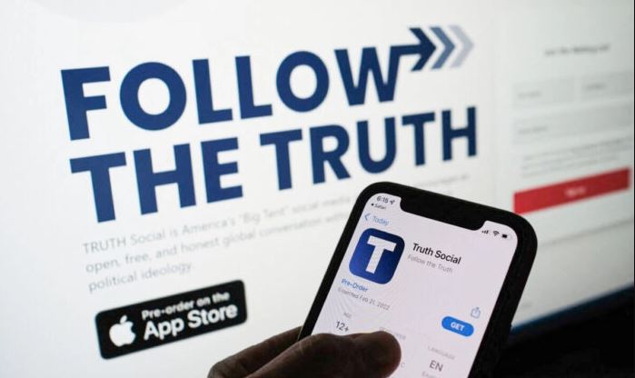 Una persona comprueba en la tienda de aplicaciones de un smartphone "Truth Social" -propiedad de Trump Media & Technology Group- con su página web en la pantalla de un ordenador, en Los Ángeles, California, el 20 de octubre de 2021. (Chris Delmas/AFP vía Getty Images)