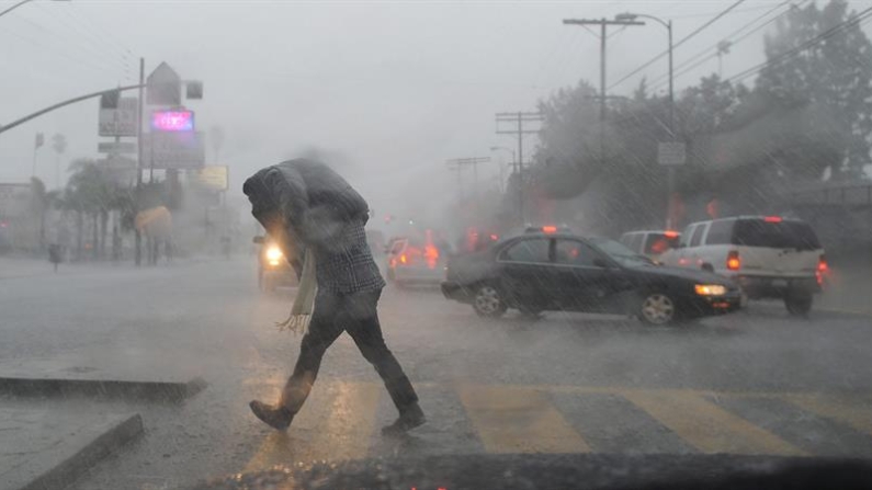 Imagen de archivo de un transeúnte que trata de cubrirse de la lluvia mientras cruza una calle en medio de una alerta de tornado. EFE/Andrew Gombert 