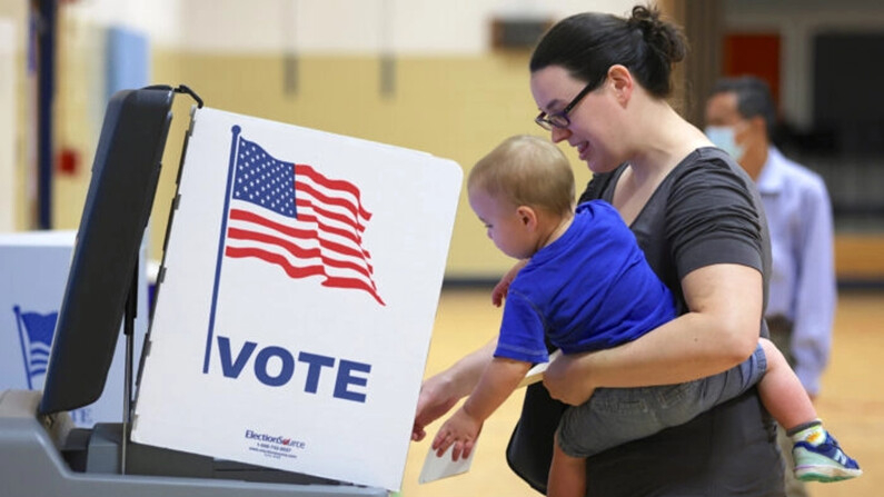 Una votante deposita su papeleta con su hijo en un colegio electoral de la Escuela Primaria Rose Hill durante las elecciones primarias de mitad de mandato, en Alexandria, Virginia, el 21 de junio de 2022. (Alex Wong/Getty Images)
