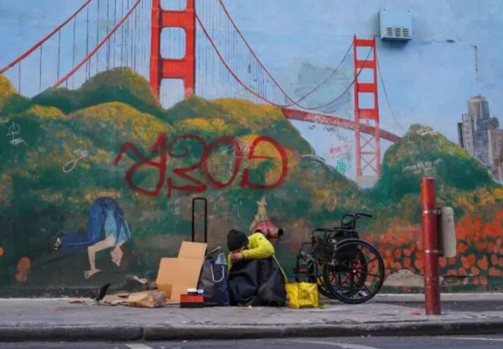 Una persona sin hogar recostada contra un mural del puente Golden Gate en el centro de San Francisco el 11 de noviembre de 2023. (Loren Elliott/AFP vía Getty Images)