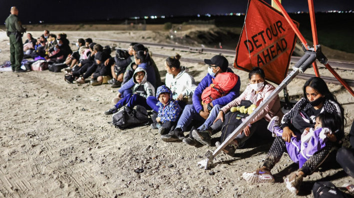Inmigrantes ilegales esperan a ser procesados por agentes de la Patrulla Fronteriza tras cruzar desde México, con la barrera fronteriza entre Estados Unidos y México al fondo, en Yuma, Arizona, el 23 de mayo de 2022. (Mario Tama/Getty Images)