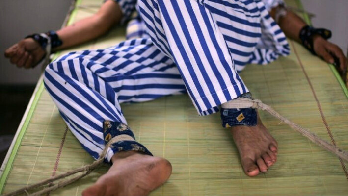 Un paciente mental yace en una cama con brazos y piernas atados en el Hospital Psiquiátrico Anxian, en la provincia de Sichuan, China, el 24 de agosto de 2008. El régimen chino también utiliza hospitales psiquiátricos para detener y castigar a los disidentes. (China Photos/Getty Images)