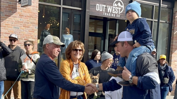 El candidato republicano al Senado de los EE.UU. por Montana, Tim Sheehy, con uno de sus hijos a hombros, saluda a la gente a lo largo de la ruta del Desfile de Bienvenida de la Universidad Estatal de Montana en octubre de 2023 en Bozeman. (Tim Sheehy para Montana)