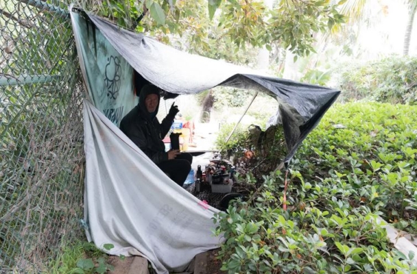 Un indigente sentado en su tienda de campaña a las afueras del cuartel H. (Jane Yang/The Epoch Times)