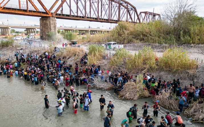 Inmigrantes ilegales esperan en el Río Grande una abertura en la barrera de alambre de cuchillas, para cruzar a Estados Unidos, en Eagle Pass, Texas, el 25 de septiembre de 2023. (Andrew Caballero-Reynolds/AFP vía Getty Images)