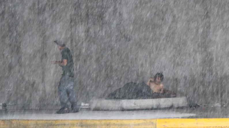 Dos habitantes de calle se protegen de la lluvia en una céntrica avenida de Monterrey (México). Fotografía de archivo. EFE/ María Julia Castañeda
