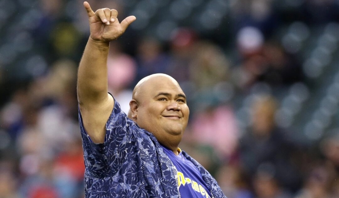 El actor Taylor Wily, también conocido como Teila Tuli, hace un gesto a los fanáticos después de realizar el primer lanzamiento ceremonial antes de un partido de béisbol entre los Marineros de Seattle y los Rangers de Texas en Seattle, el 14 de junio de 2014. (Elaine Thompson/Foto AP, archivo)