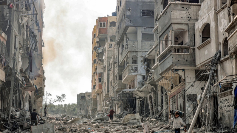 Un hombre lleva un cilindro de gas propano mientras camina entre escombros que llenan una calle en el área de refugiados de Jabalia en la ciudad de Gaza el 11 de octubre de 2023, en el quinto día de batallas entre el grupo terrorista Hamas e Israel. (Mahmud Hams/AFP via Getty Images)