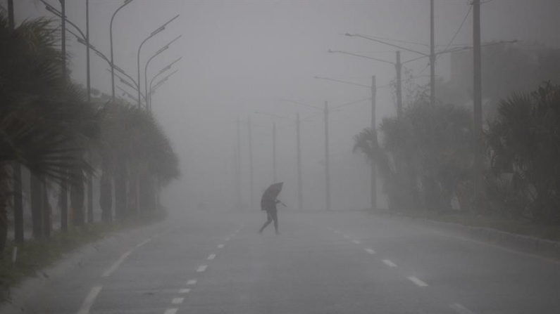 Una persona cruza hoy una avenida bajo una fuerte lluvia debido al paso de una tormenta tropical. Fotografía de archivo. EFE/Orlando Barría