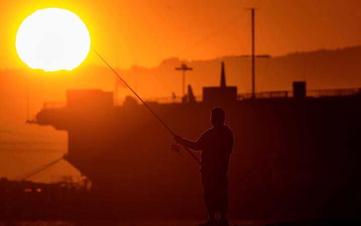 Un hombre pesca en un embarcadero de Alameda, California, mientras el sol se pone sobre la bahía de San Francisco, el 1 de julio de 2024. (Noah Berger/AP)